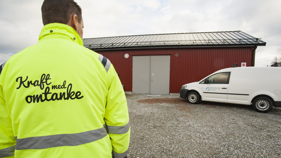 En person med reflexjacka och texten "Kraft med omtanke" står framför en av Sölvesborg energis bilar.