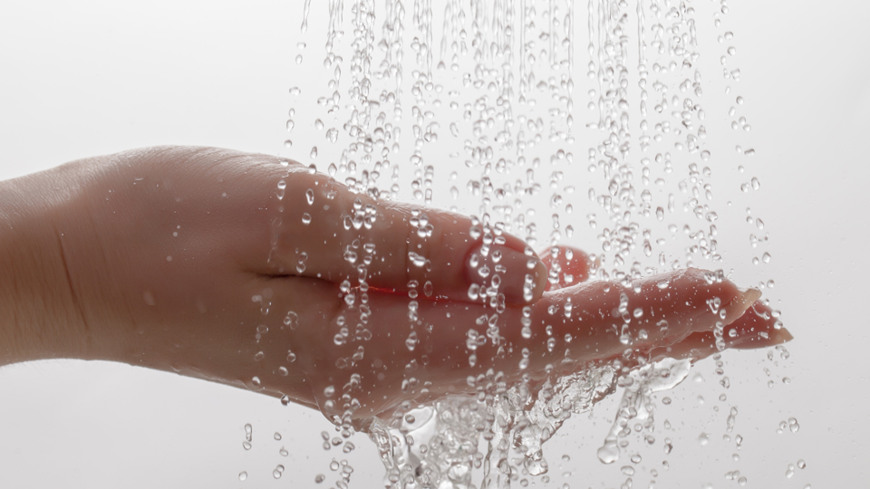 En kupad hand under flera vattenstrålar mot en ljus bakgrund.