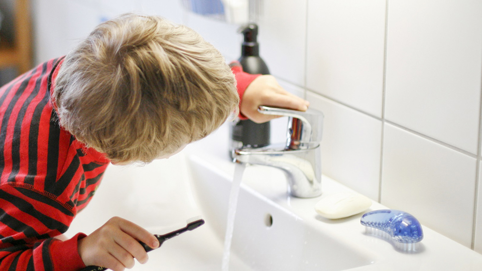 Barn som dricker vatten ur kranen i badrummet efter att ha borstat tänderna.